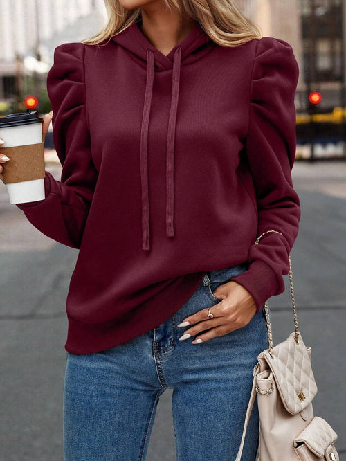 Burgundy cotton-blend hoodie featuring slim-fit silhouette, puff sleeves, and drawstring hood worn with blue jeans.