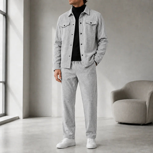 Man wearing a light gray casual button-front jacket with matching trousers, a black turtleneck sweater, and white sneakers.