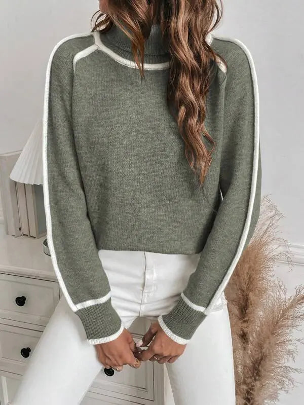 Olive green turtleneck sweater with white contrast piping, ribbed cuffs, and a soft knit texture worn with white jeans.
