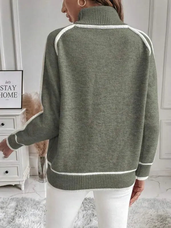 Olive green turtleneck sweater with white contrast piping, ribbed cuffs, and a plush knit texture worn with white pants.