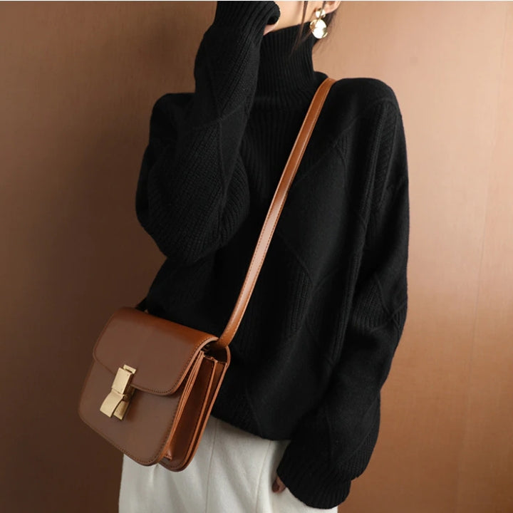 Black wool turtleneck sweater featuring a raised diamond-pattern knit, ribbed collar, and cuffs, worn with a brown crossbody bag.
