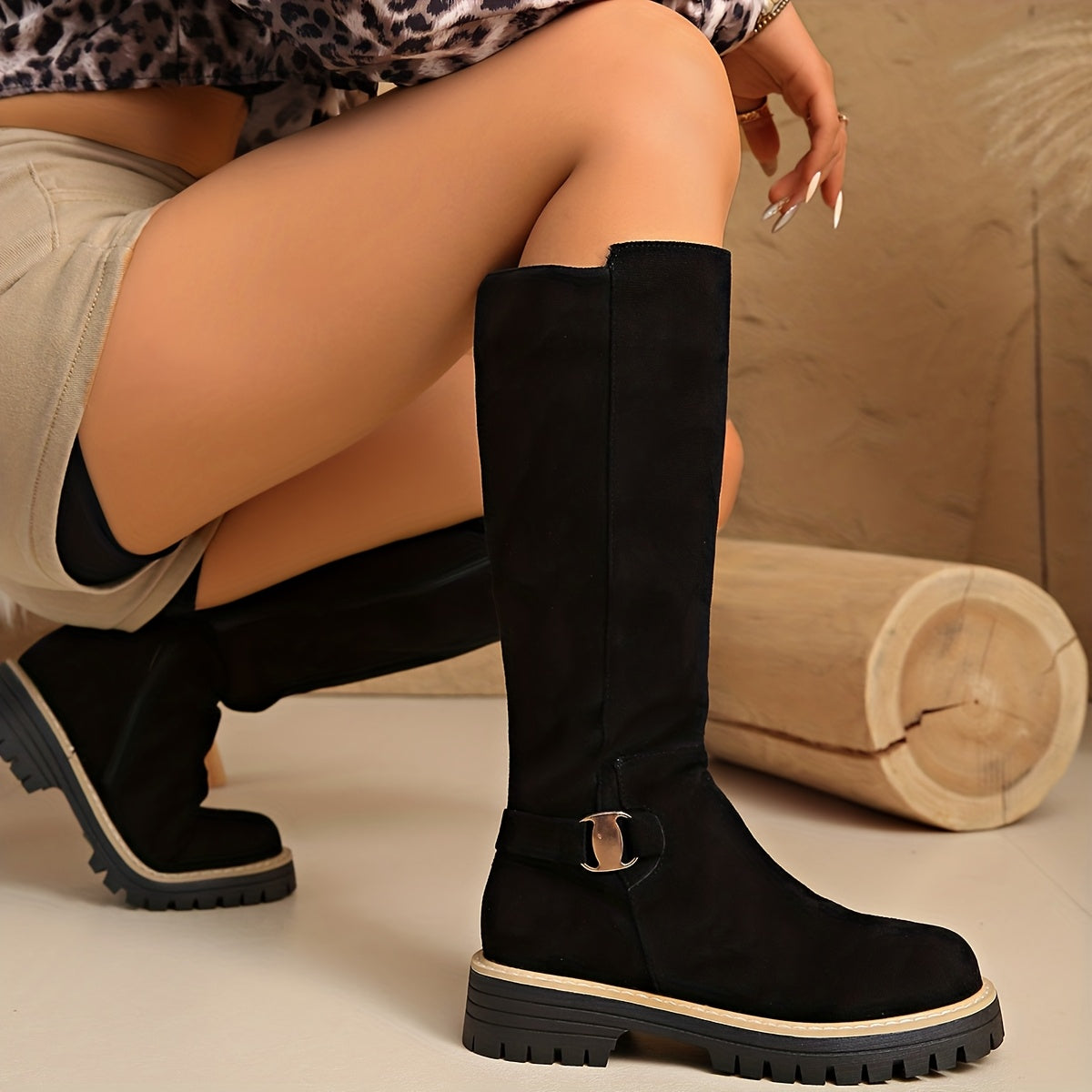 Black napped knee-high boots with a chunky lug sole, stitched welt trim, and a small ankle buckle.