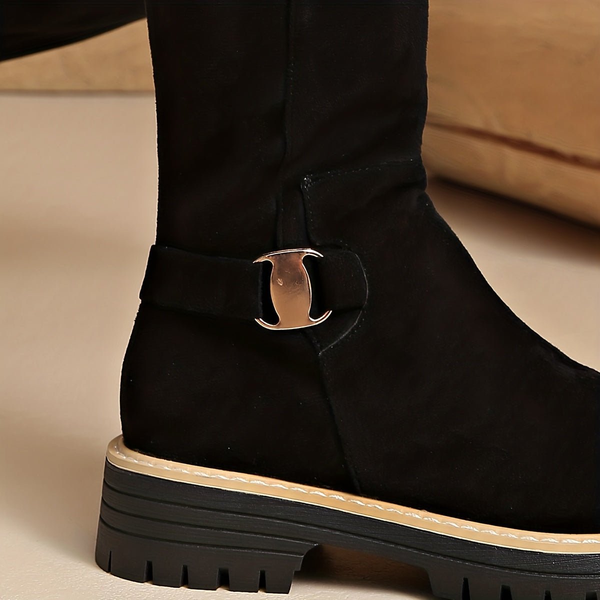 Black napped knee-high boot with a chunky lug sole, stitched welt trim, and a metallic ankle buckle detail.