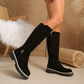 Black napped knee-high boots with a chunky lug sole, stitched welt trim, and a side ankle buckle.