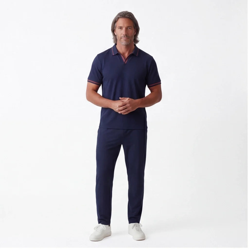 Man wearing a navy short-sleeve polo shirt with matching navy drawstring pants and white sneakers in a full-body studio portrait.