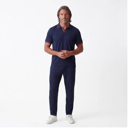 Man wearing a navy short-sleeve polo shirt with matching navy drawstring pants and white sneakers in a full-body studio portrait.