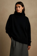 Black oversized turtleneck sweater with a relaxed fit, dropped shoulders, and ribbed cuffs, paired with a gray skirt.