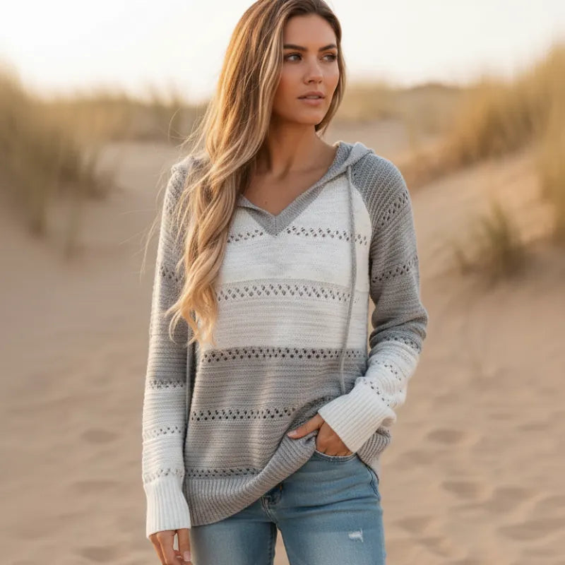 Color-block striped knit hooded pullover with eyelet crochet trim, V-neck, and ribbed cuffs on a beach at sunset.