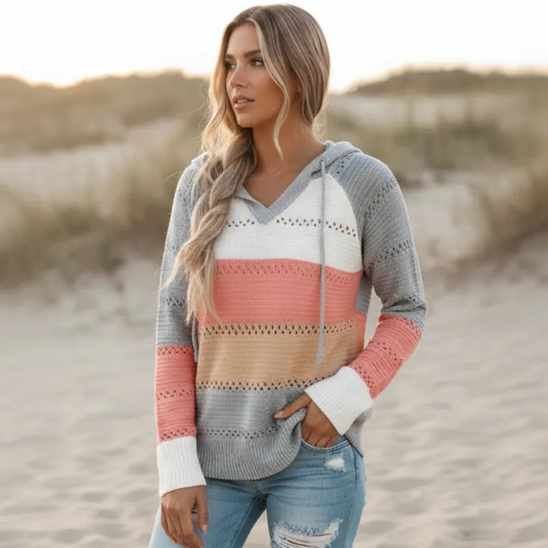 Color-block striped knit hooded pullover with eyelet crochet trim, V-neck, and ribbed cuffs on a beach at sunset.