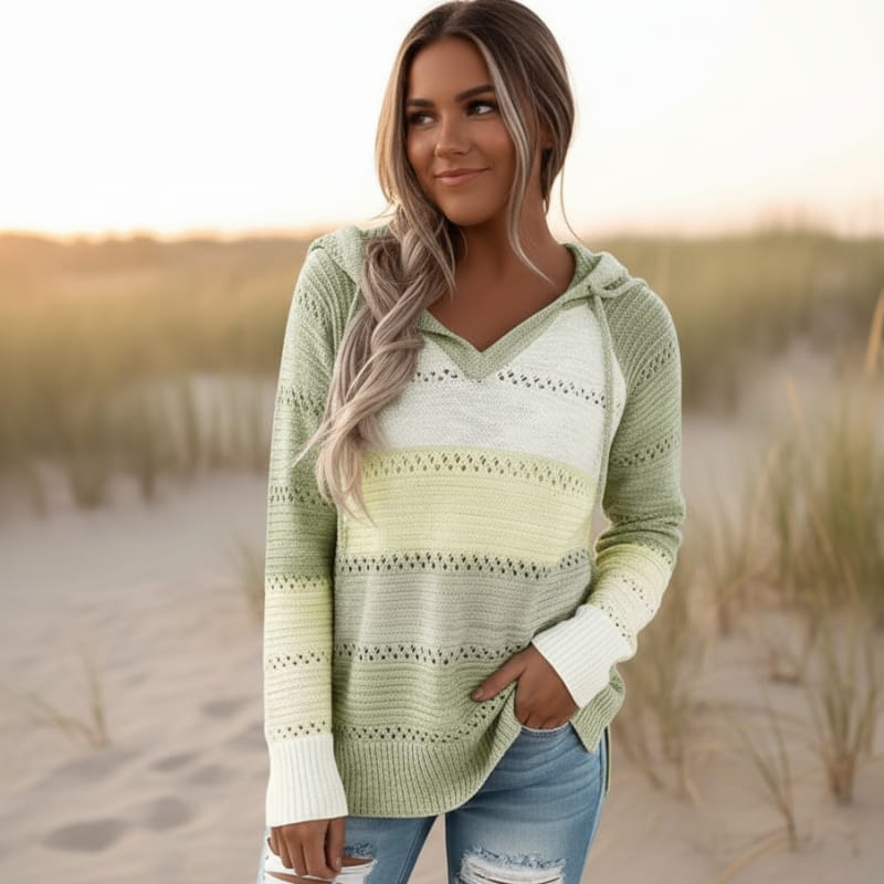 Green and yellow color-block hooded knit sweater with eyelet crochet trim, V-neck, and ribbed cuffs worn on a beach.
