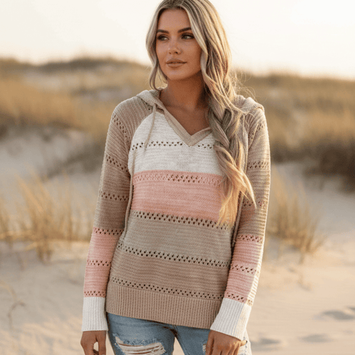 Color-block striped hooded sweater in neutral tones with eyelet crochet trim, V-neck, and ribbed cuffs on a beach.