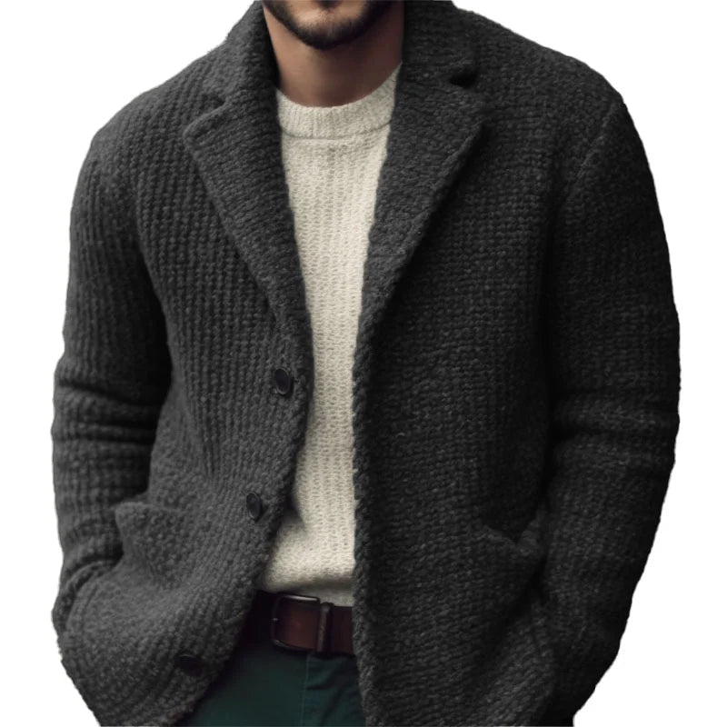 Charcoal grey textured knit cardigan with a notch collar, button front, and patch pockets layered over a cream sweater.