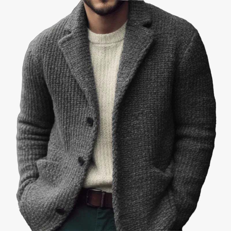 Charcoal grey textured knit cardigan with a notch collar, button-front closure, and patch pockets over a cream sweater.