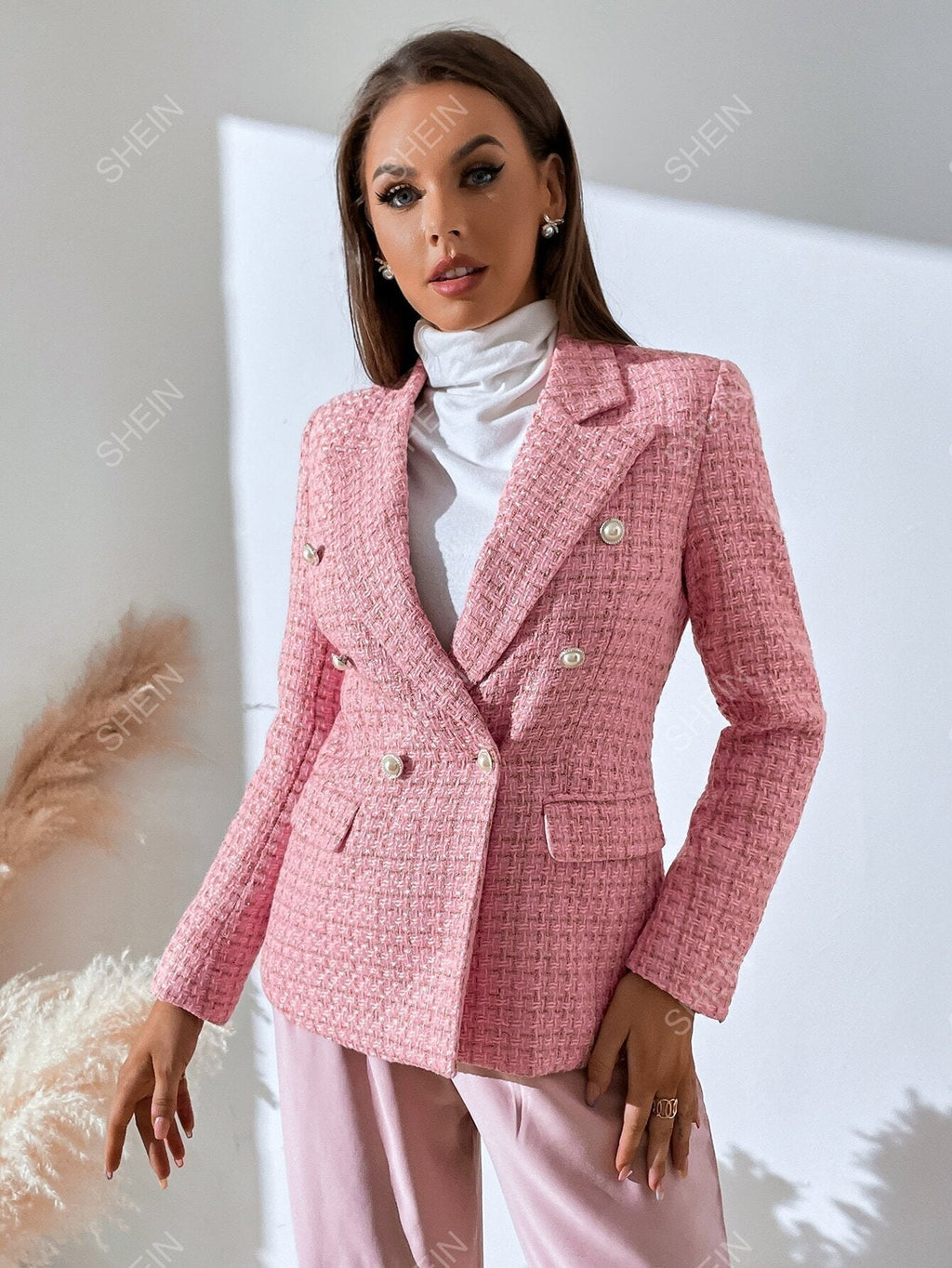 Pink tweed double-breasted blazer with notched lapels, accent buttons, and a tailored fit worn over a white turtleneck.
