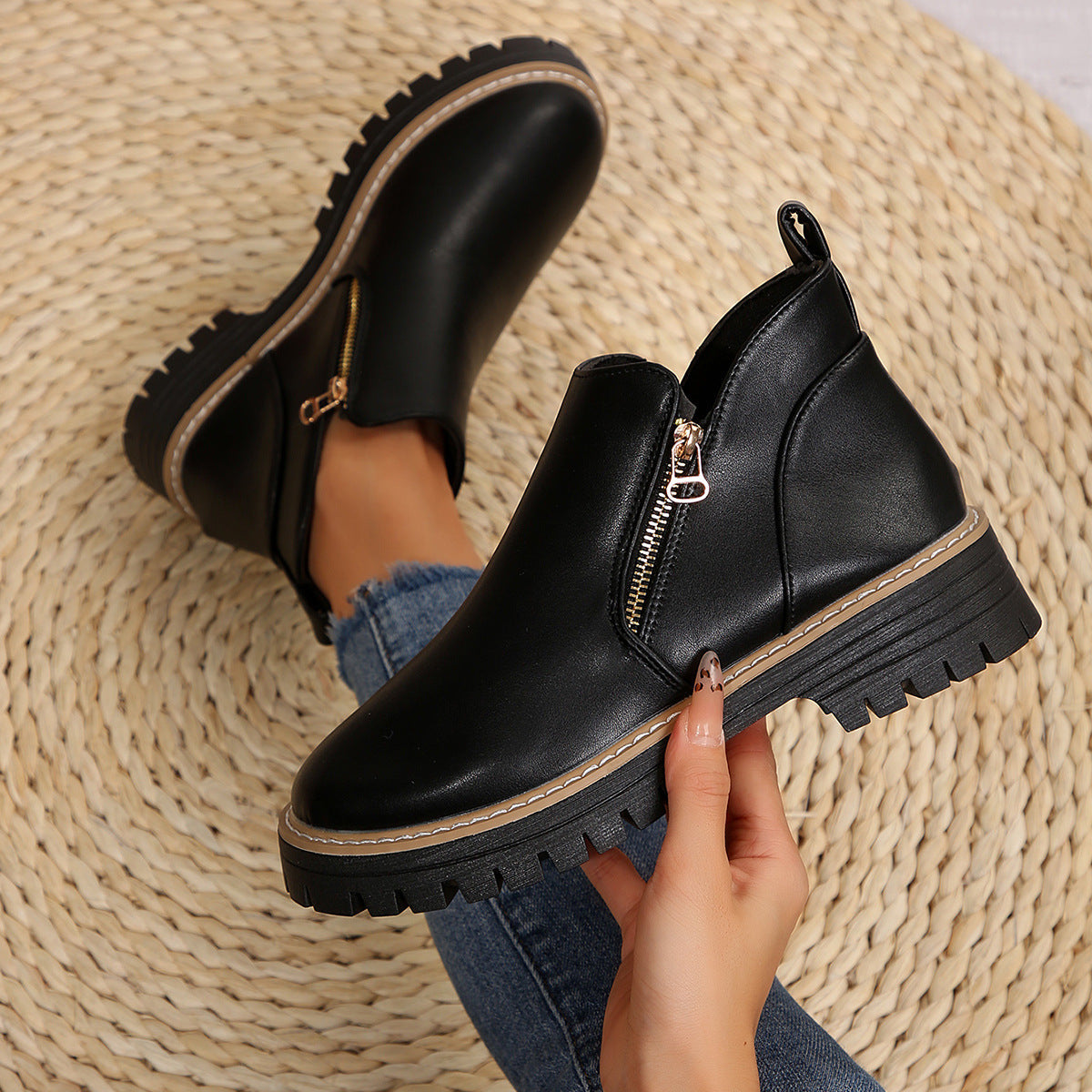 Black ankle boots with side zips, round toes, and thick notched tread soles on a textured woven background.
