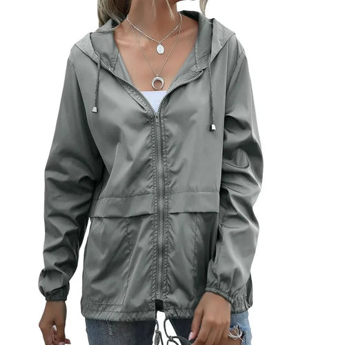 Woman wearing an olive green hooded windbreaker jacket featuring a full-zip front, adjustable hood, and elastic cuffs.