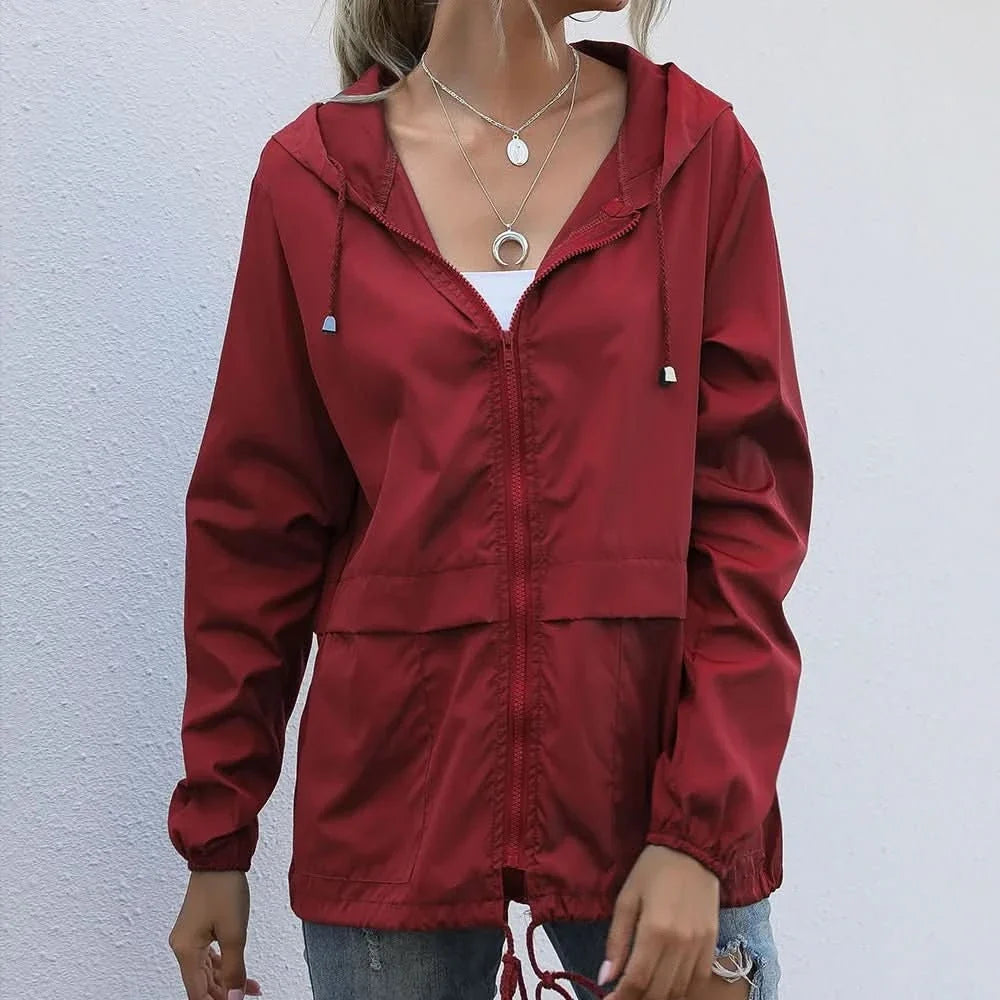 Woman wearing a red hooded lightweight windbreaker jacket with a zip-front closure, adjustable drawstrings, and long sleeves.