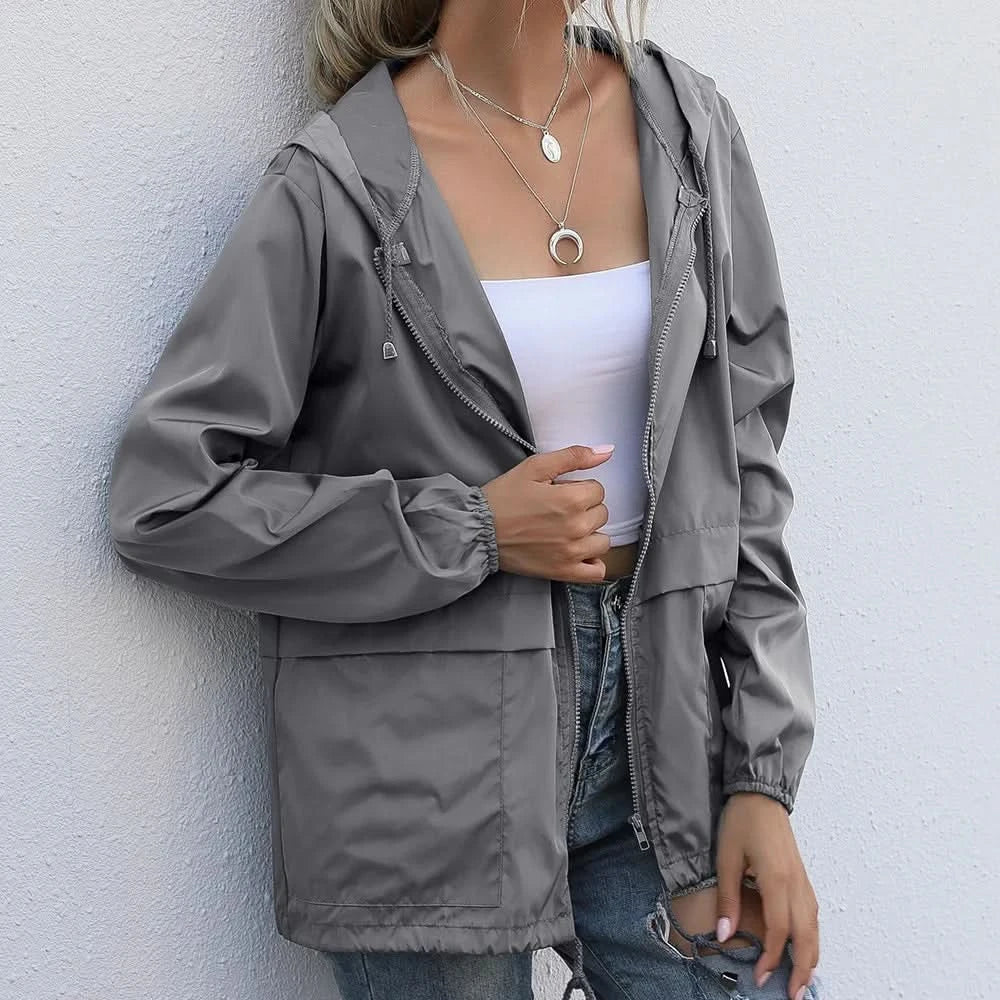 Woman wearing a gray hooded windbreaker jacket with a full-zip front, adjustable hood, and lightweight design.
