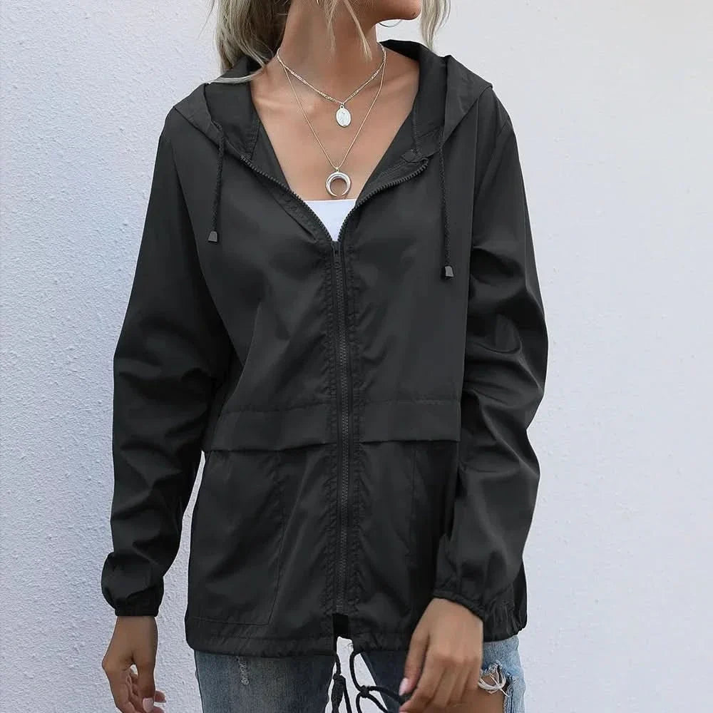 Woman wearing a black hooded lightweight windbreaker jacket featuring a zip-front closure, adjustable drawstrings, and elastic cuffs.