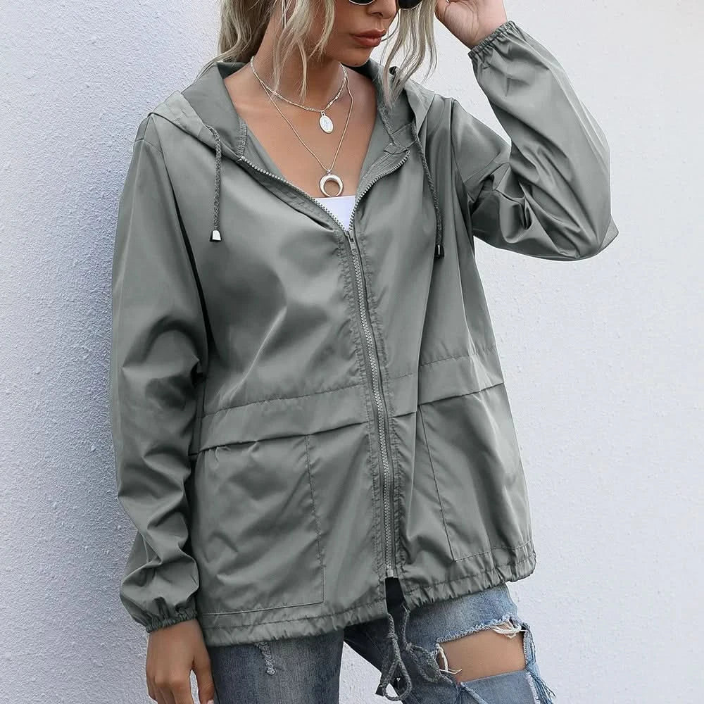 Woman wearing an olive green hooded lightweight windbreaker jacket with a zip-front closure, adjustable drawstrings, and elastic cuffs.