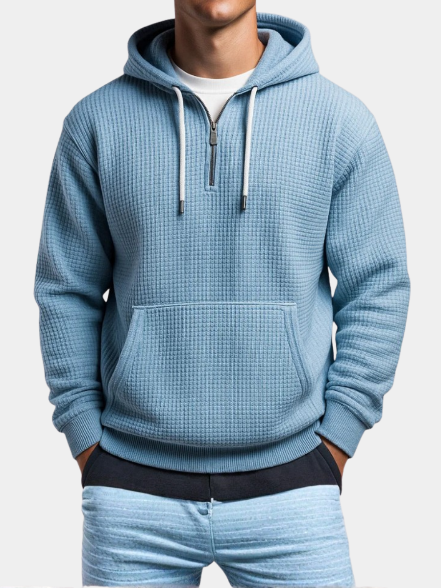 Light blue waffle knit pullover hoodie with a kangaroo pocket, adjustable drawstrings, and a relaxed fit, paired with light blue jeans.
