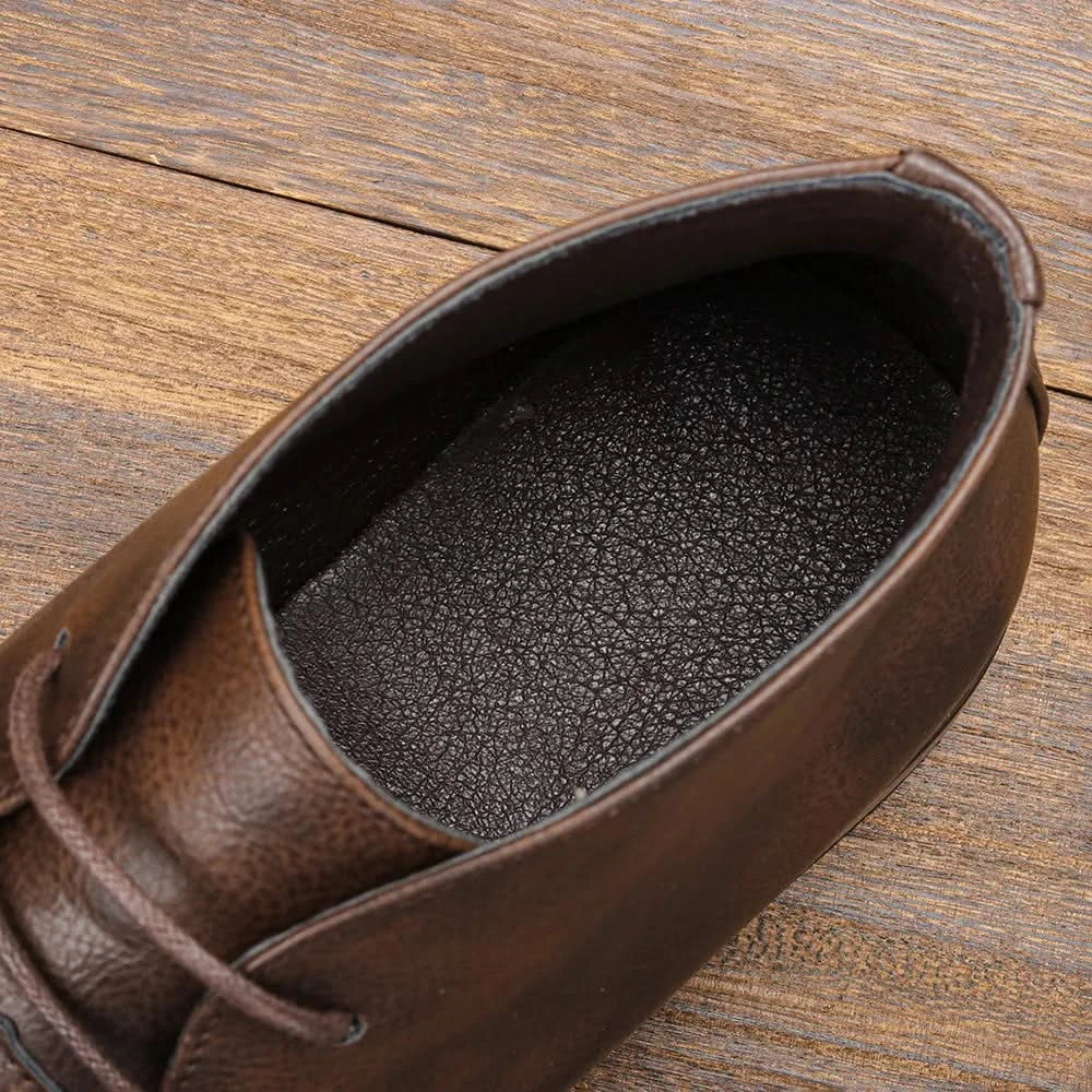 Dark brown grained leather chukka boot with a cushioned insole and lace-up closure on a wooden surface.
