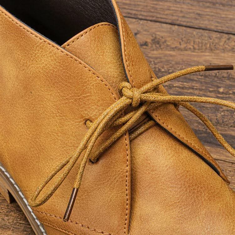 Tan grained leather chukka boots featuring three-eyelet lace-up closure, visible welt stitching, and a low stacked heel.