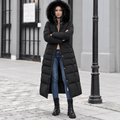 Black maxi puffer coat with box quilting, plush-trim hood, and snap placket, worn over jeans and boots.