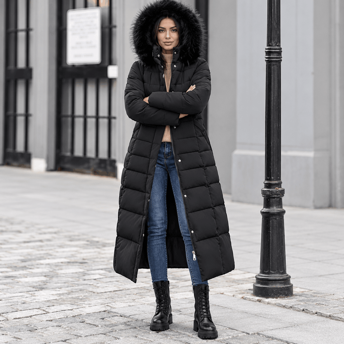 Black maxi puffer coat with box quilting, plush-trim hood, and snap placket, worn over jeans and boots.