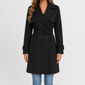 Black double-breasted trench coat with a belted waist, storm flap, and adjustable buckle cuff straps in a smooth finish.