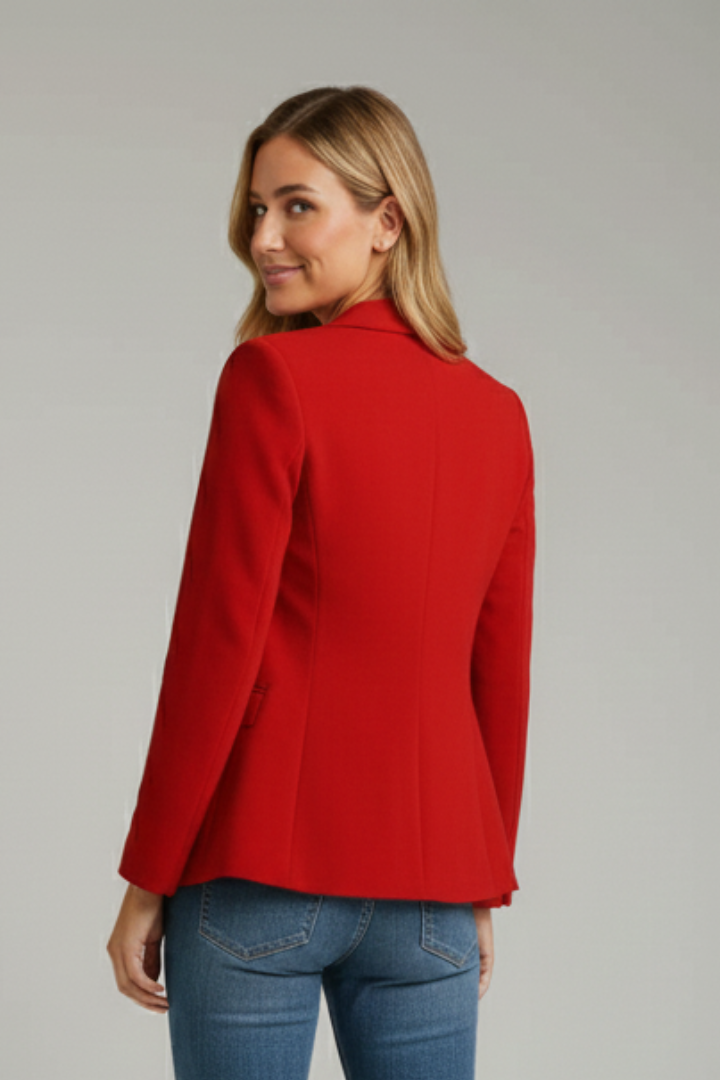 Tailored red blazer with a structured shoulder and notched lapel, worn over blue denim jeans.