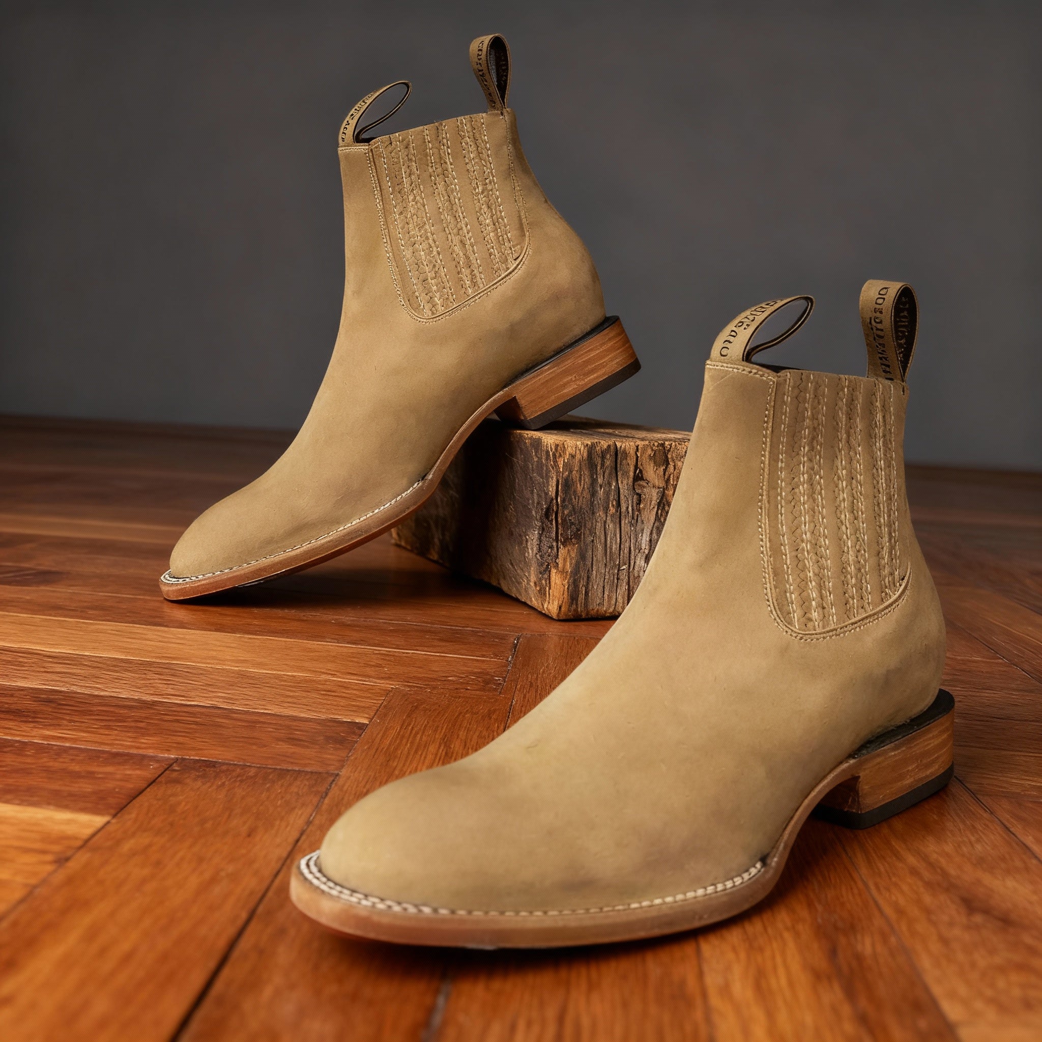 Tan suede western ankle boots with pointed toes, elastic side panels, and stacked block heels on a wooden floor.