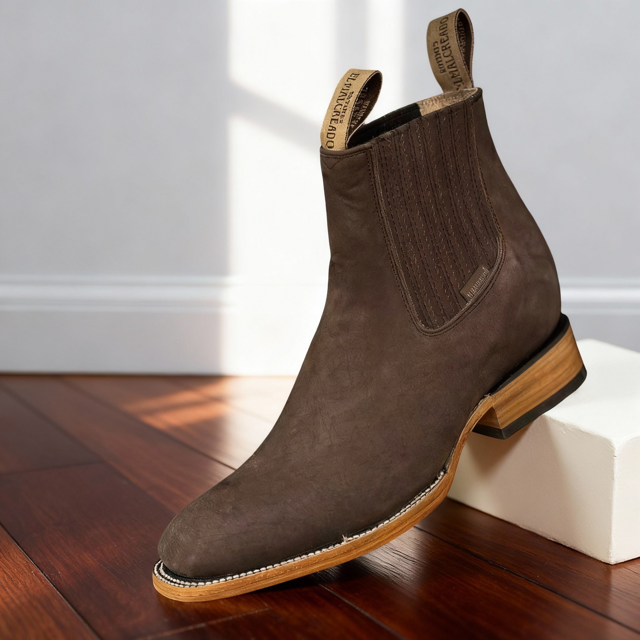 Dark brown suede western ankle boot with a pointed toe, elastic side panels, and a stacked wooden block heel.