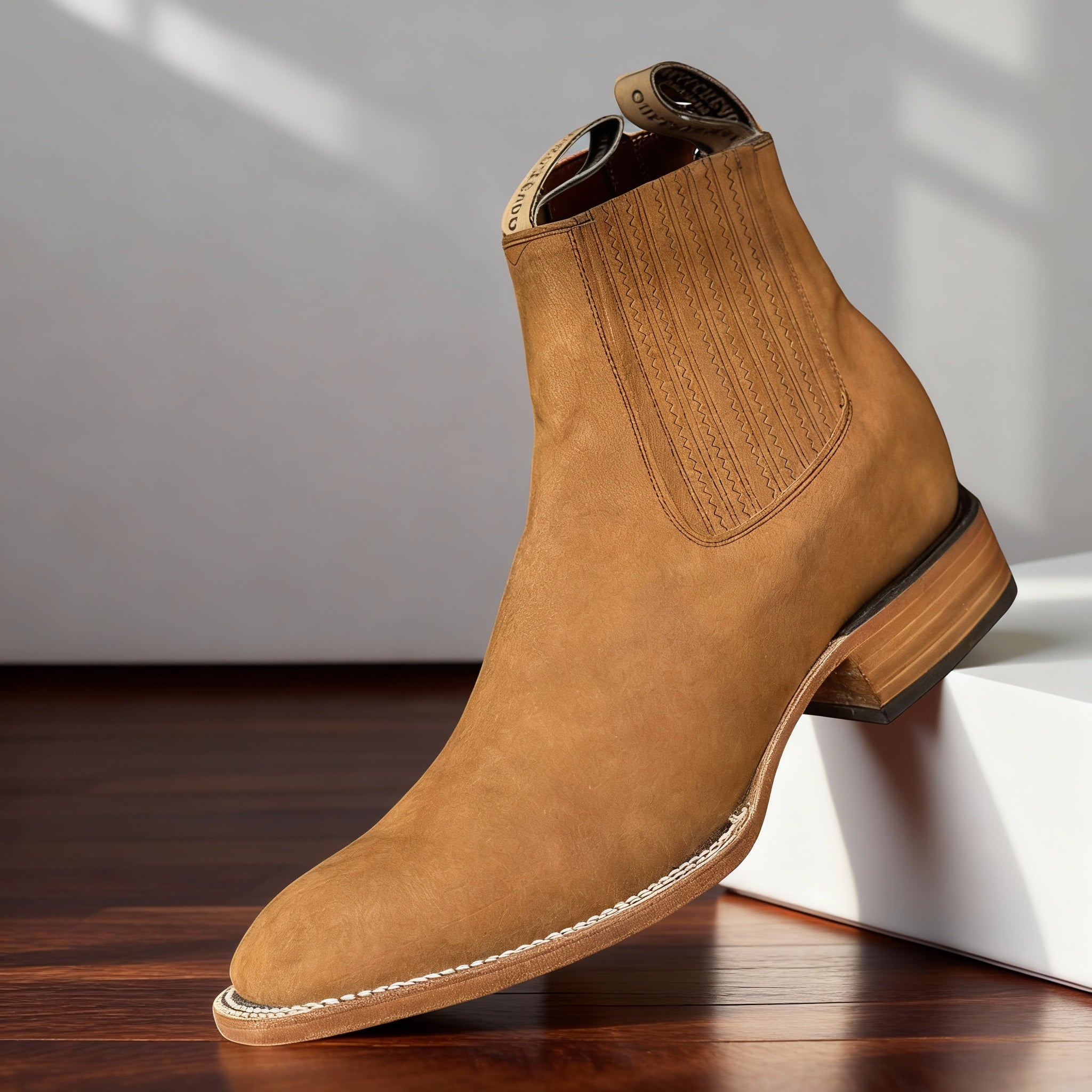Tan suede western ankle boot with a pointed toe, elastic side gore, and a stacked block heel on a wooden surface.