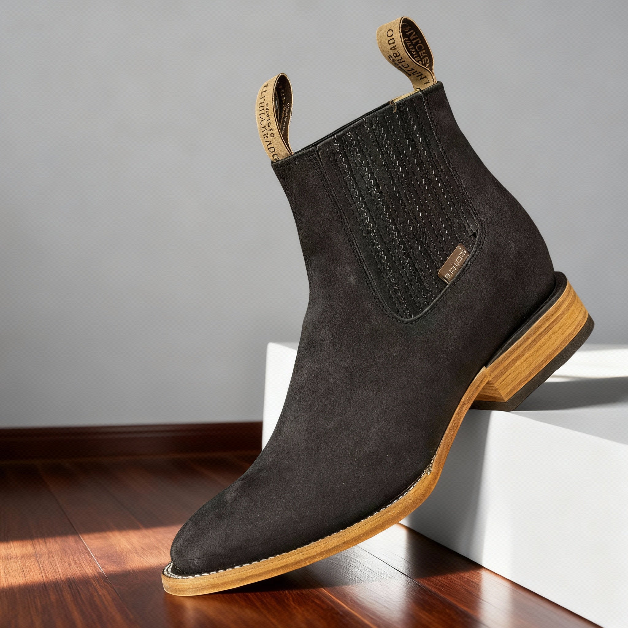 Black suede western ankle boot with a pointed toe, elastic side panels, and a light-toned stacked wooden heel.