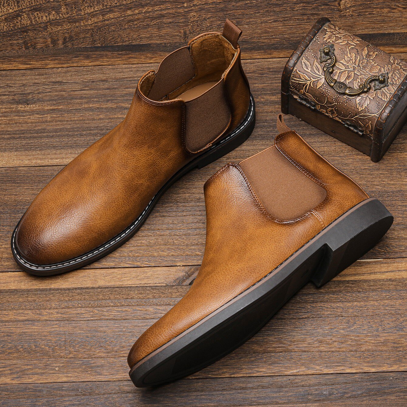 Tan leather Chelsea boots with round toes, elastic side gores, and black block heels on a rustic wooden surface.