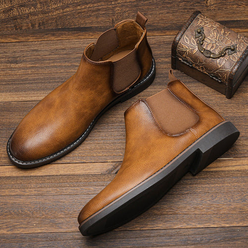 Tan leather Chelsea boots with round toes, elastic side gores, and black block heels on a rustic wooden surface.