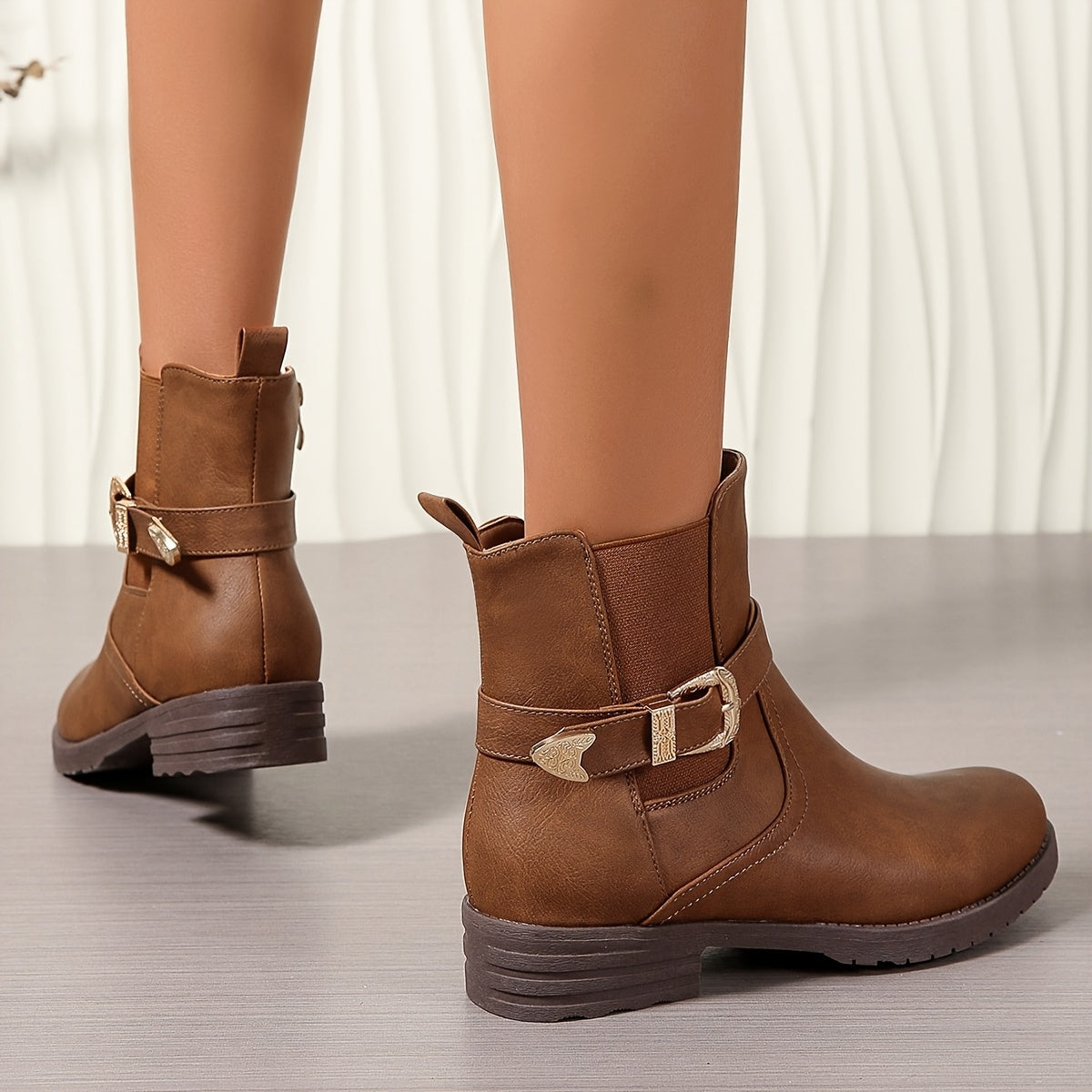Brown western ankle boots featuring an engraved gold buckle strap, elastic Chelsea gore panels, and a rear pull tab.