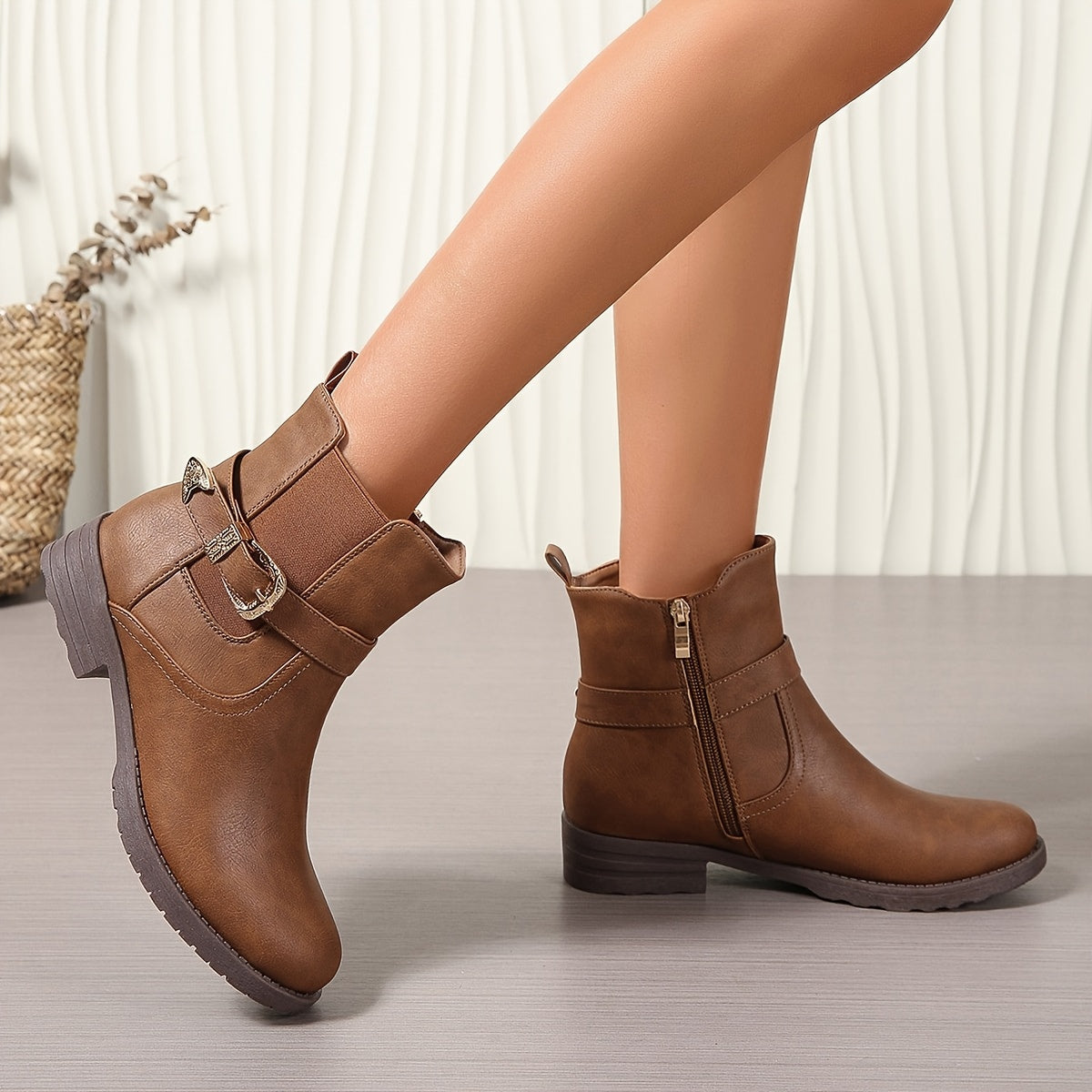 Brown western ankle boots featuring an engraved buckle strap, side zipper, and block heel on a textured synthetic leather.