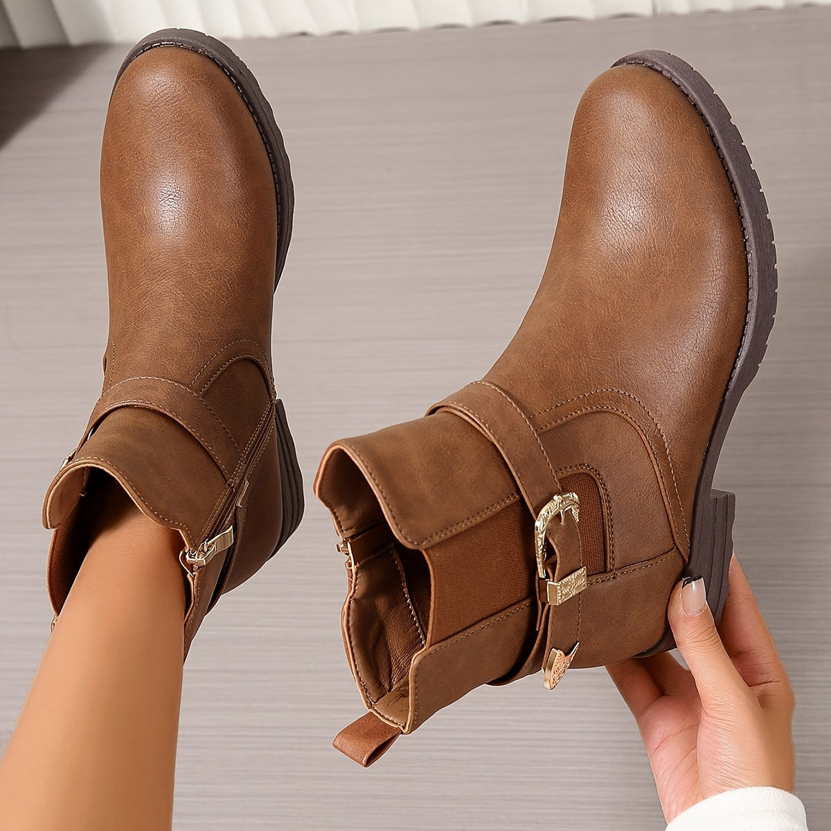 Brown western ankle boots featuring an engraved buckle strap, elastic gore side panels, and a sturdy block heel.