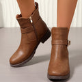 Brown western ankle boots with an engraved buckle strap, side zipper, and block heel worn on a neutral surface.