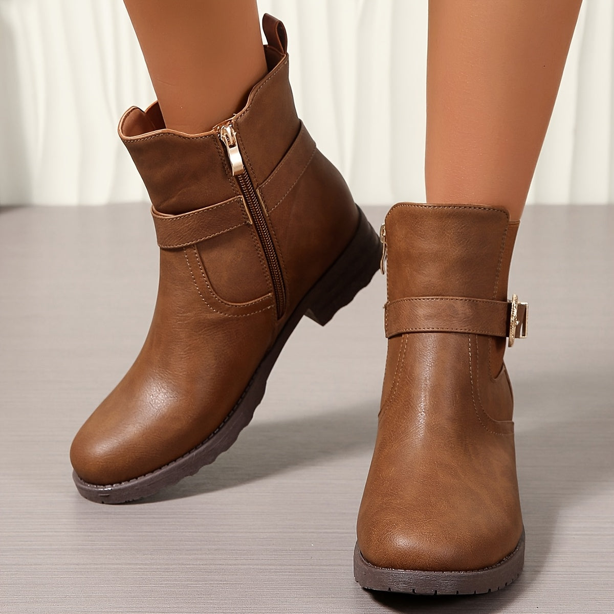 Brown western ankle boots with an engraved buckle strap, side zipper, and block heel worn on a neutral surface.