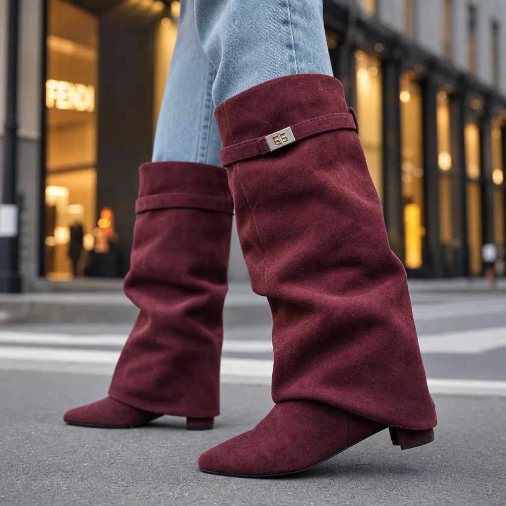 Burgundy slouch knee-high suede boots with pointed toes and mid block heels, worn with light blue jeans in an urban setting.
