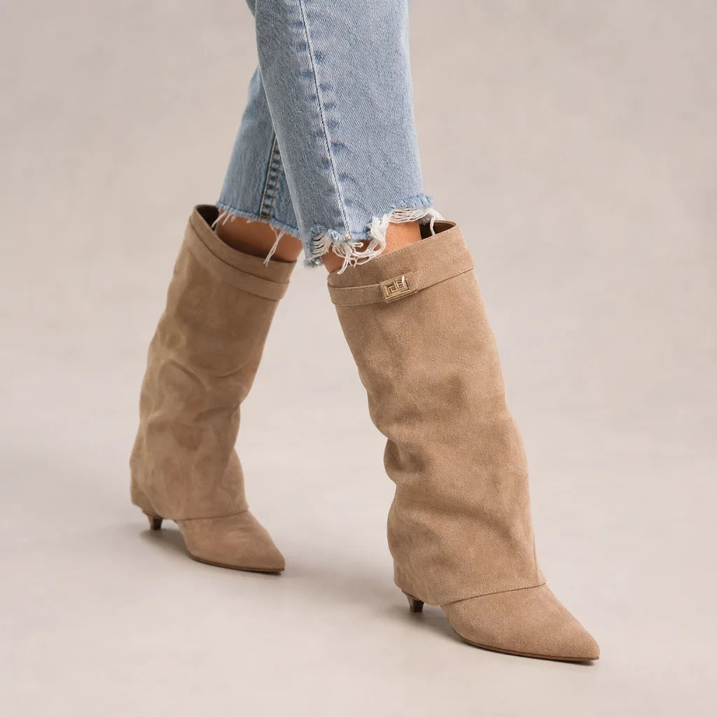 Taupe slouch knee-high suede boots featuring pointed toes and mid block heels, styled with light blue jeans.