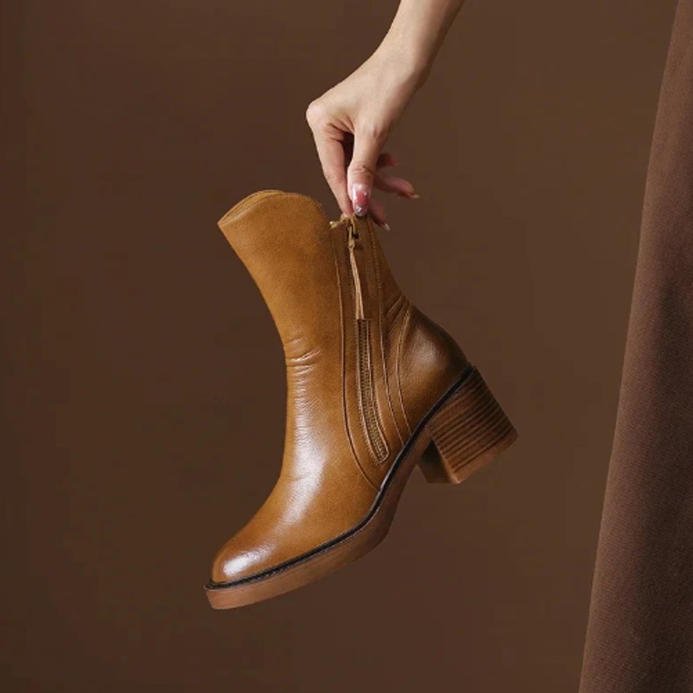 Tan grained ankle boot with a full-length side zip, round toe, and a sturdy stacked block heel against a brown background.