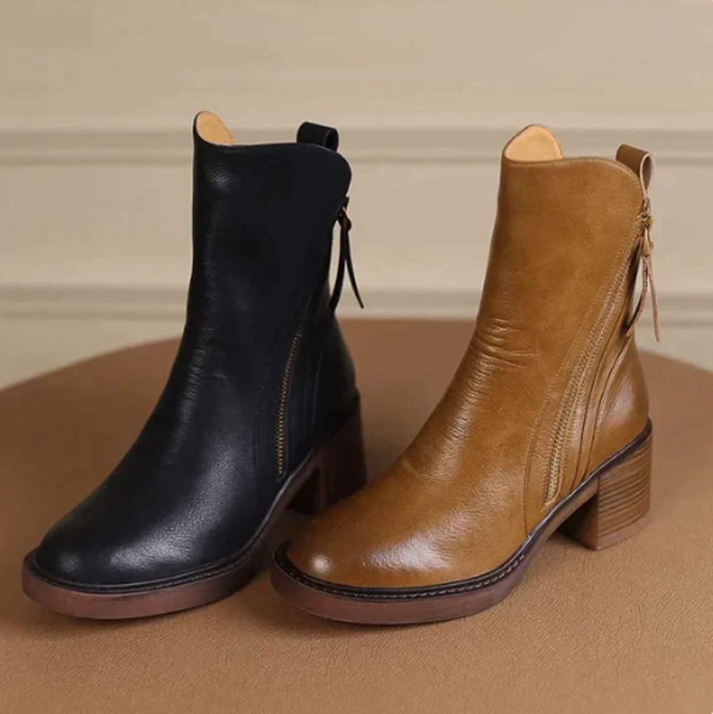 Black and tan grained leather ankle boots with side zips, stacked block heels, and knotted back ties on a round table.