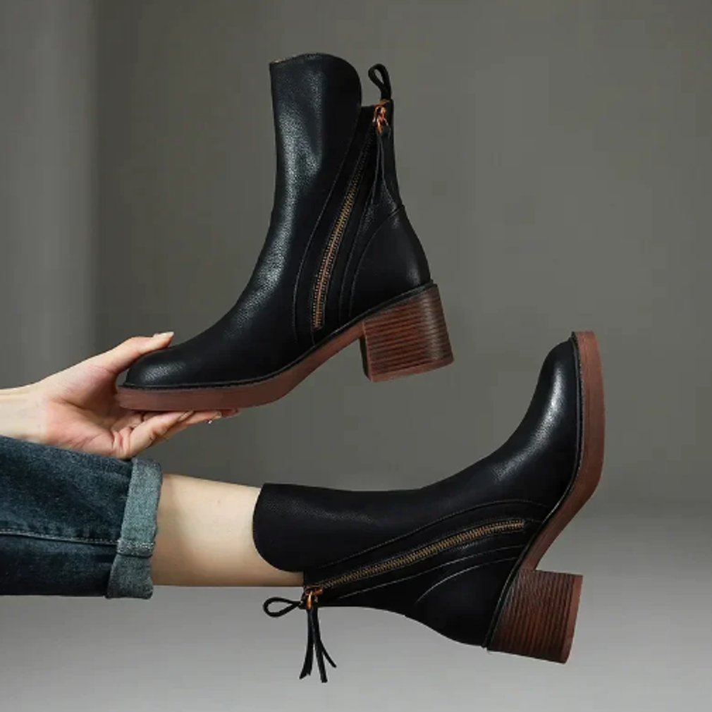 Black grained ankle boots with side zips, stacked block heels, and knotted back ties held against a neutral background.
