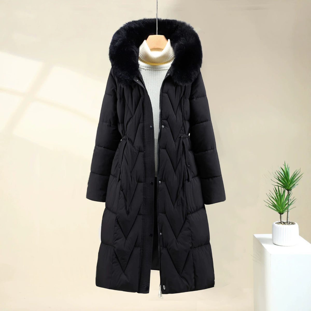 Black Chevron-Quilted Longline Puffer Coat featuring a plush-trimmed hood, chevron quilting, drawstring waist, full-length front closure, and longline silhouette.