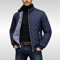 Man wearing a navy diamond-quilted zip-up jacket with a stand collar, fleece lining, black turtleneck sweater, and blue jeans.