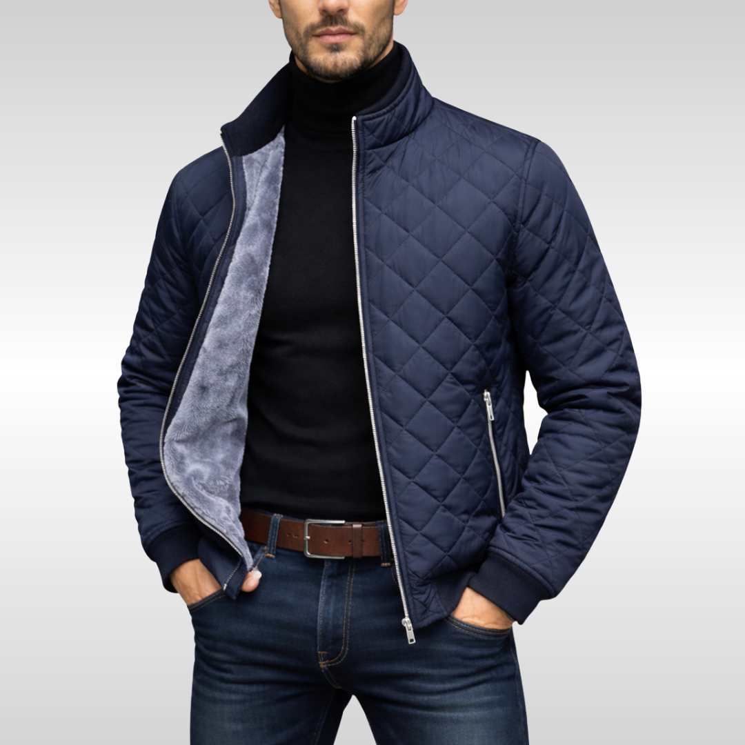 Man wearing a navy diamond-quilted zip-up jacket with a stand collar, fleece lining, black turtleneck sweater, and blue jeans.